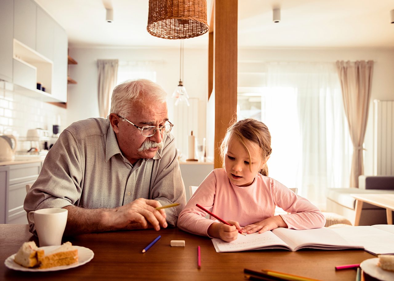 Grandpa helping his granddaughter with homework at the dining table
